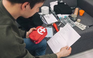 Genç adam evrak, su, yiyecek, ilk yardım çantası ve hayatta kalmak için gerekli diğer eşyalarla dolu bir çanta hazırlıyor.