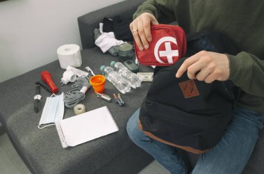 Genç adam evrak, su, yiyecek, ilk yardım çantası ve hayatta kalmak için gerekli diğer eşyalarla dolu bir çanta hazırlıyor.