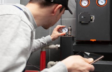 Teknisyen elinde tabletle kazan dairesindeki ısıtma sistemini kontrol ediyor.