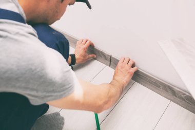 Worker is finishing floor installation and installing skirting board 