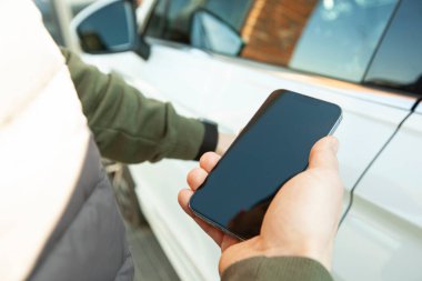 Man holding mobile phone next to door of his car in the street