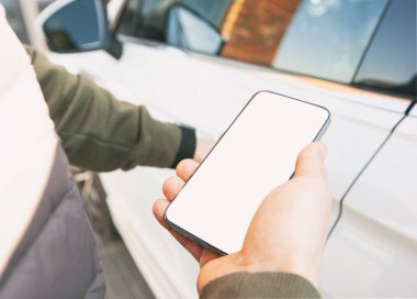 Man holding mobile phone with blank screen next to door of her car in the street
