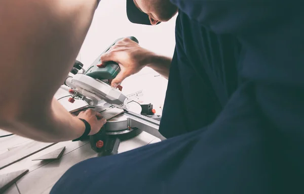 A worker cuts a skirting board made of fibreboard with a miter saw