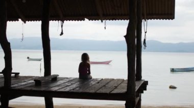 Yalnız kız denizin kenarında bir platformda oturuyor.