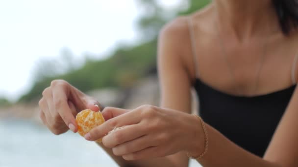 Unerkennbare Frau schält die Schale einer Mandarine — Stockvideo