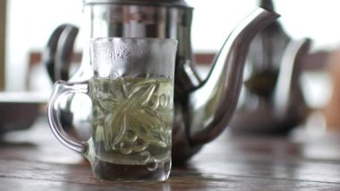 Bardakta yeşil çay ve masada çaydanlık.