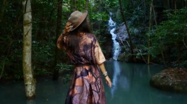 A girl in a hat and Asian clothes in a fabulously mystical landscape near a waterfall.
