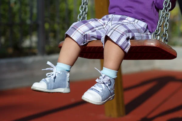 Fötter av oigenkännlig baby svängande på lekplats — Stockfoto