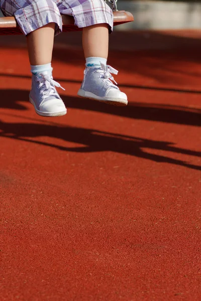 Feet of a little child swinging on playground — Stock Photo, Image