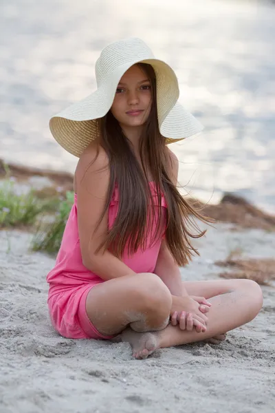 Schattig jong meisje in hoed zittend op het strand — Stockfoto