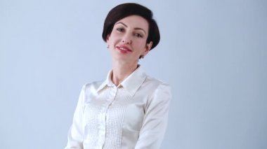 Stüdyoda arkadaş canlısı bir iş kadını pozu. Resmi giyinmiş genç bir kadın model, video için dostane bir gülümsemeyle kırmızı ruj. İpek gömlekli güzel beyaz kadın kamerayla gülümsüyor.