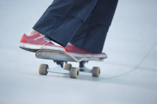 Skater girl rolling on concrete ramp in outdoor skate park. Female skateboarder athlete wearing red shoes