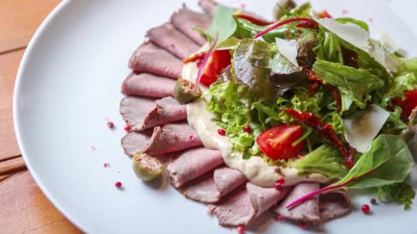 スライス肉と新鮮な野菜とおいしい牛肉のサラダのストックフードビデオは グルメレストランでテーブルの上に白いセラミックプレート上で提供 — ストック動画