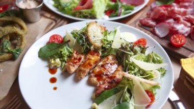 Akdeniz restoranında beyaz tabakta servis edilen kızarmış ekmek, parmesan peyniri ve mikro sebzeli tavuk Sezar salatası.