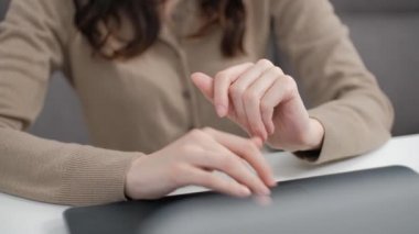 Evde, oturma odasındaki beyaz masanın arkasında dizüstü bilgisayarda çalışan bedava mızraklı kadın eli. Çalışmak için not defteri kullanan kadın çalışanın stok görüntüleri. 4K 'da Royalty Free Stock videosu çekilmiştir.