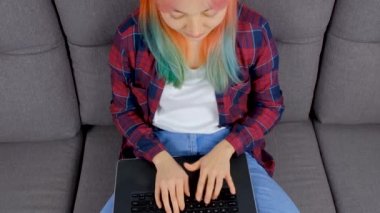 Serbest çalışan kız, tecrit altındaki evinde kanepesinde otururken bilgisayarla uzaktan çalışıyor. Dizüstü bilgisayarda yazı yazan ücretsiz mızrak işçisi. Evden çekilen bağımsız çalışma videosu stok videosu 4K