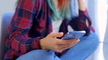 Genç kız, sosyal medya uygulamalarını taramak için modern cep telefonu kullanıyor. Saçları boyalı, günlük kıyafetler giyen ve internete akıllı telefon takan genç bir kadının stok videosu. 4K içinde stok video klibi