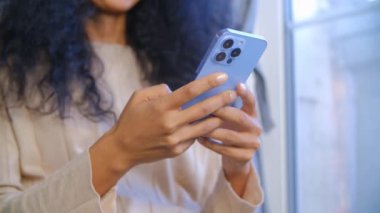 Genç, yetişkin Afrikalı bir kadın, evde kilitli bir şekilde modern cep telefonu kullanıyor. Siyah kadın internette geziniyor ve üç kameralı, modaya uygun akıllı telefondaki sosyal medya uygulamasında yeni beslemeler yapıyor. Taşınabilir internet kavramı