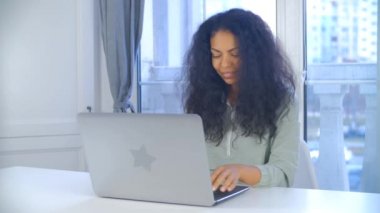 Bilgisayarda çalışan odaklanmış siyahi bir kadın. Kapalı evde dizüstü bilgisayarda yazan profesyonel serbest çalışan bir kadın. Afrikalı kişi 4K video 'da gülümseyerek uzaktan beleş mızrak kullanıyordu.
