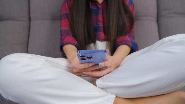 年轻妇女在家里坐在沙发上使用手机 在现代智能手机上使用4K股票视频中的三重摄像头输入女孩消息 并有缩放效果 — 图库视频影像