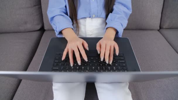 ラップトップコンピュータに手を入力します リビングでソファーに座りながらノートパソコンで働く若いアジア人女性の4Kストック動画 フリーランスの女性は インターネット上で遠くの仕事やオンライン教育を行う — ストック動画