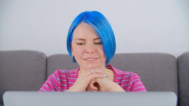 Mutlu gülüşlü güzel beyaz kadın 4K stok videosunda bilgisayar ekranından okuyor. Kafkasyalı, şirin bir kadın. Mavi saçlı. Tecrit sırasında laptopla öğreniyor.