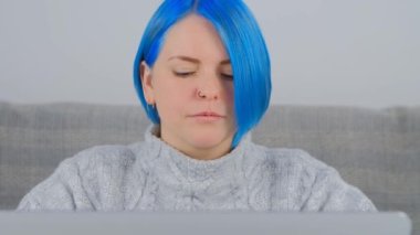 Kapatma sırasında evde dizüstü bilgisayarla çalışan boyalı mavi saçlı genç kadın. Beyaz kadın uzaktan çalışıyor. Millenial kişi hızlı internet bağlantısı ve dizüstü bilgisayarla çevrimiçi öğreniyor