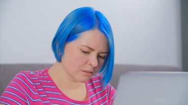 Bilgisayarda çalışan odaklanmış beyaz kadın. 4K stok videosunda dizüstü bilgisayarında mavi boyalı saçları olan güzel bir beyaz kadın. Uzaktan çalışma için dizüstü bilgisayar kullanan profesyonel serbest yazar