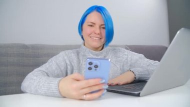 Genç beyaz kadın, boyalı mavi saçlı cep telefonuyla internette geziniyor. Kafkasyalı mutlu kadın üç kameralı akıllı telefon cihazıyla çevrimiçi iletişim kuruyor. Sosyal medya uygulaması kullanarak gülümseyen kişi