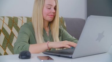 Sarışın kadın evdeki tecritte çalışırken dizüstü bilgisayarda klavye kullanıyor. Yüzünde kırbaç izi ve protez göz olan beyaz kadın internete bağlı defter bilgisayarı üzerinde çalışıyor.