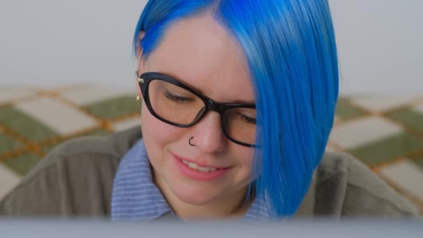コンピュータ上で働く青い髪を染めた幸せなオタクの女性4K映像 ロックダウン中にラップトップで遠く離れたフリーランスの仕事をしている美しいミレニアル世代 ノートに入力するフリーランスの女性 — ストック動画