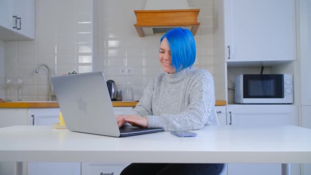 ノートPcとインターネット接続でオンライン学習幸せな若い白人女性 4Kストックビデオでラップトップ上で働く陽気な白人女性 染めた青い髪のタイプの文字で微笑む人 — ストック動画