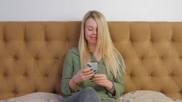 寝室で現代の携帯電話を使用して美しい白い女性 スマートフォンでインターネットニュースフィードを閲覧する白人女性をリラックスさせました 4Kの携帯電話上のソーシャルメディアアプリとオンラインで通信する人 — ストック動画