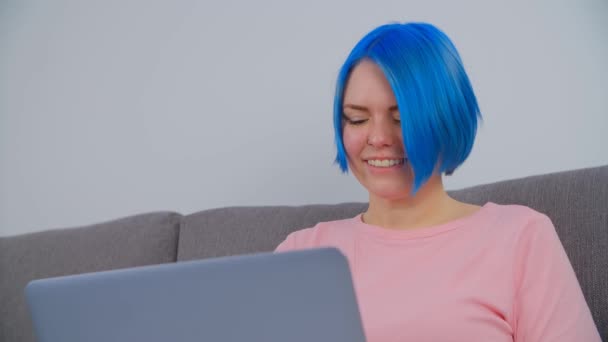 明るい歯の笑顔でノートパソコンで働く青い髪の幸せな白い女性 ロックダウン中に自宅でノートブック上でフリーランスの仕事を行う若い創造的な専門家 かわいい女性の入力上のコンピュータ — ストック動画