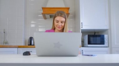 Evde dizüstü bilgisayarla çalışan odaklanmış genç bir kadın. Güzel beyaz kadın tecrit sırasında defter bilgisayarında çalışıyor. Neşeli Kafkasyalı kişi 4K stok görüntülerinde online çalışıyor.