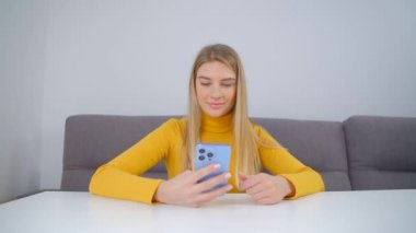 Akıllı telefon kullanan mutlu genç bir kadın. Modern cep telefonunda internette gezinen güzel beyaz kadın. Tecrit sırasında cep telefonundan sosyal medya uygulaması ile çevrimiçi iletişim kuran güzel sarışın kişi
