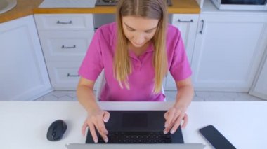 İnternette çalışan serbest çalışan bir kadın. Laptop klavyesinde yazan genç sarışın kadın. 4k stok videosunda hızlı internet bağlantısı ve dizüstü bilgisayarı olan beyaz kişi uzak çalışma veya eğitim yapıyor