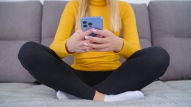 Çevrimiçi iletişim için cep telefonu kullanan genç bir kadın. Modern akıllı telefon cihazında sosyal medya uygulamasında mesaj yazan beyaz kadın. Kurye başvurusu üzerine mesaj yazan kişi kanepede oturan beyaz
