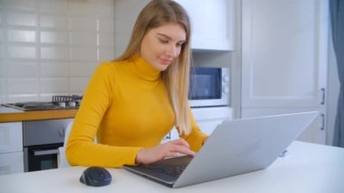 Tecrit sırasında evden bilgisayar başında çalışan güzel bir serbest çalışan kadın. Laptop klavyesinde sarı saçlı, yazı yazan mutlu beyaz kadın. Uzaktan bağımsız iş yapan neşeli bir insan.