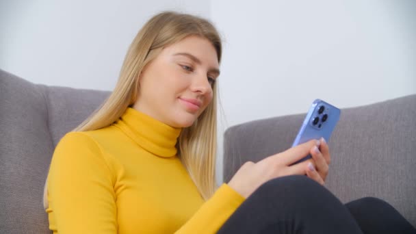 幸せな若い女性が携帯電話にメッセージを入力します オンライン通信やエンターテイメントのための近代的なスマートフォンを使用して美しいブロンドの女性 ソーシャルメディアアプリでコミュニケーションをとる陽気な人 — ストック動画