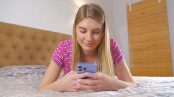 寝室の携帯電話のアプリケーションにかなり白い女性の入力メッセージ 美しい若いです大人白人女性通信オンラインで現代的なスマートフォンやソーシャルメディアアプリでクローズアップ4Lビデオ — ストック動画