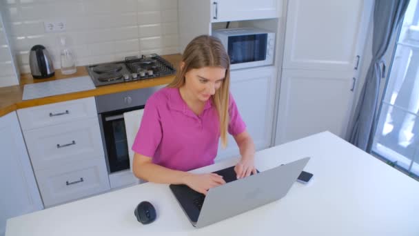 ロックダウン時に自宅でラップトップコンピュータを入力するオンライン学生 若いブロンドの女性がノートパソコンで4Kストックビデオで働いています 高速インターネット接続で遠くの仕事をしているフリーランスの女性 — ストック動画