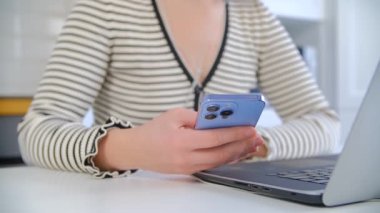 Serbest çalışan kadın modern cep telefonundan internet haberlerine bakıyor. 4K video içerisindeki tecrit sırasında eğlence ve iletişim için mavi akıllı telefon aygıtı kullanan bir kadın.