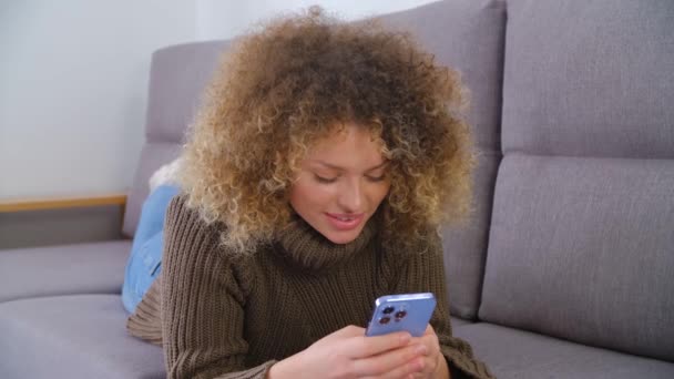 卷曲的白人妇女躺在沙发上用智能手机打字 在4K股票视频中使用现代手机进行在线交流和娱乐的漂亮白人女性 — 图库视频影像