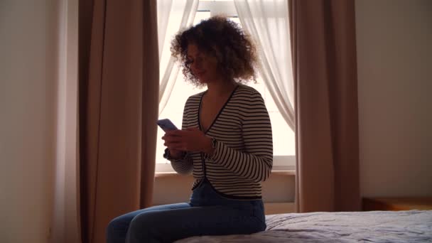 White Woman Using Mobile Phone Dark Bedroom Curly Young Adult — Stock Video