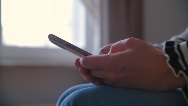 女性が携帯電話にメッセージを入力する 寝室に座っている女性とロックダウン中にオンライン通信のための近代的な黄金のスマートフォンを使用して — ストック動画
