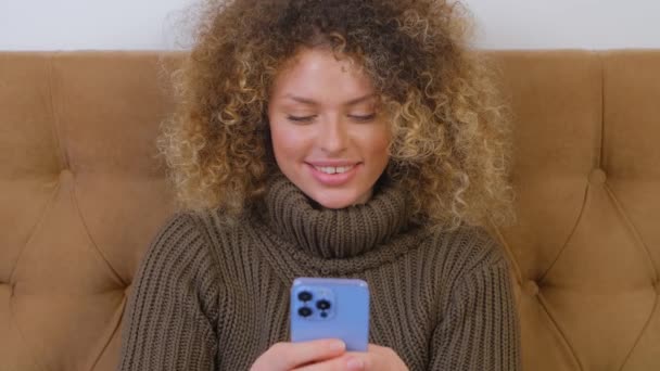 快乐的白人女性在封锁期间使用社交媒体应用进行在线交流 年轻快乐的成年女性在现代智能手机上输入消息 漂亮的卷曲人 手里拿着手机 — 图库视频影像