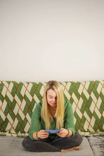 漂亮的金发白人女人玩网络游戏手机 白种人女性在家里坐在沙发上 用现代智能手机在网上玩游戏 — 图库照片
