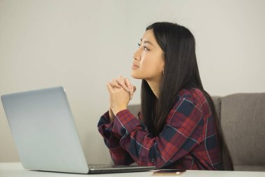 Güzel Asyalı kız evde bilgisayarla çalışıyor. Genç yetişkin girişimci kadın dizüstü bilgisayarın önünde problem çözmeyi düşünüyor. Serbest Çalışan Kadın İnternette Uzak İş Yapıyor