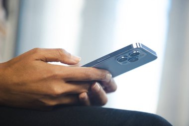 Modern mavi cep telefonunda üçlü kamerayla mesaj yazan siyahi bir kadın. Genç Afrikalı kadın çevrimiçi iletişim için yeni akıllı telefon kullanıyor.